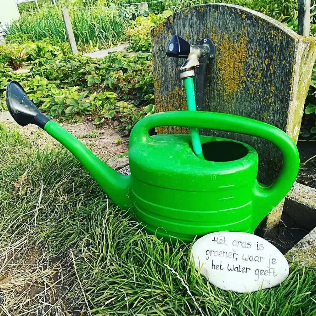 Een groene gieter bij een kraan op de tuin